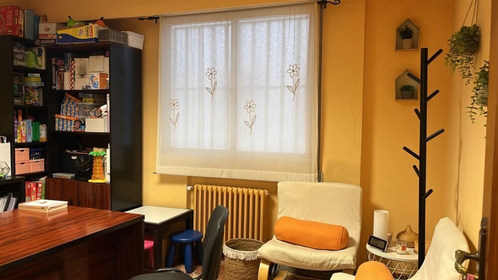 Despacho de Beatriz, con sillones junto a la ventana y estanterías de juegos para niños y adolescentes