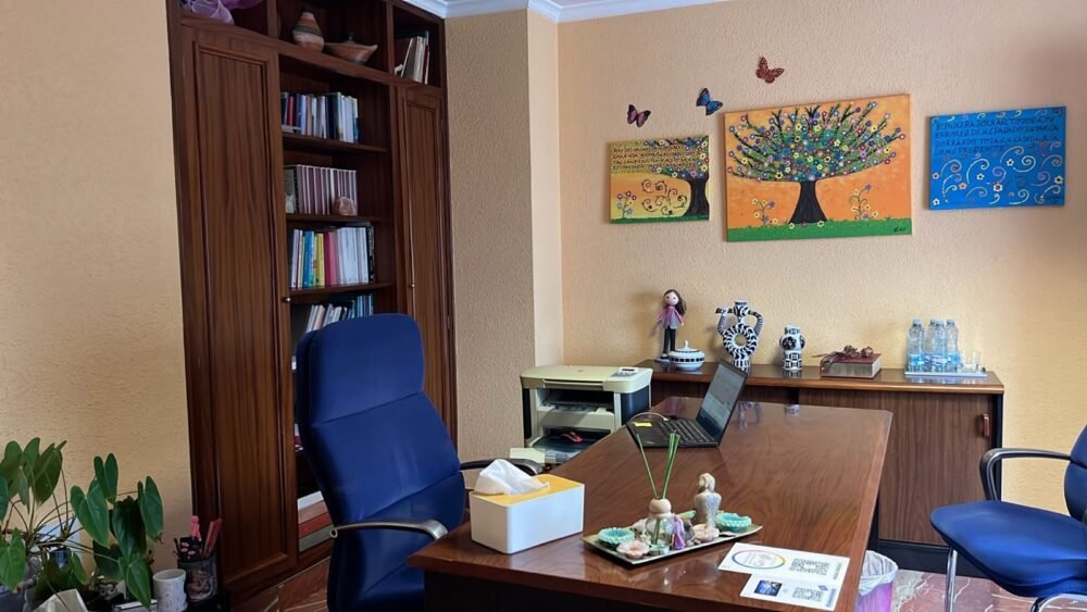Mesa del despacho de Dolores Valero, con una librería y tres cuadros de colores en la pared
